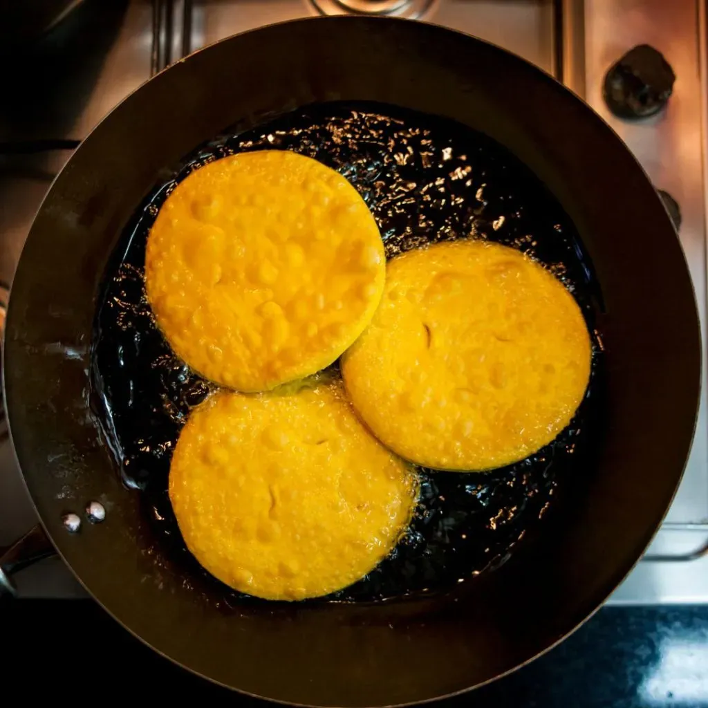Sopaipillas siendo fritas en un sarten con aceite limpio.
