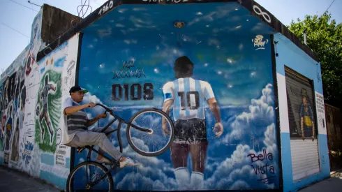 BUENOS AIRES, ARGENTINA – OCTOBER 21: A man wheelies past a mural depicting Diego Armando Maradona entering heaven with a legend that reads in spanish "Here rests god" making reference to the fact that the idol is buried one block away from the mural in Bella Vista on October 21, 2021 in Buenos Aires, Argentina. Football fans all over the country remember their late idol, who would have turned 61 on October 30. (Photo by Tomas Cuesta/Getty Images)

