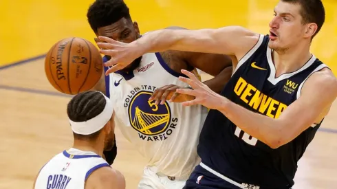 Nikola Jokic (Denver) passing the ball between Stephen Curry and Kevon Looney (Warriors). (Getty)
