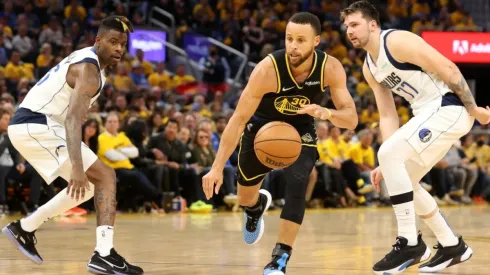 Stephen Curry #30 of the Golden State Warriors drives past Reggie Bullock #25 and Luka Doncic #77 of the Dallas Mavericks
