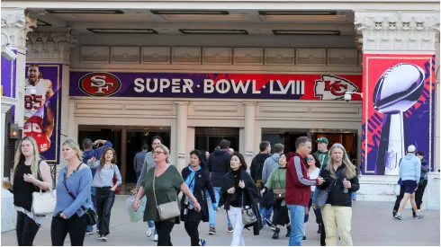 Visitors walk in front of an entrance to Caesars Palace with Super Bowl LVIII signage displayed
