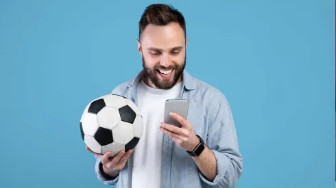 Happy young guy with soccer ball using smartphone, winning sports bet, rooting for his favorite team on blue background Contributor: Prostock-studio / Alamy Stock Photo Image ID: 2F4FPA4