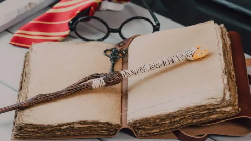 Primer plano de una varita junto a un libro de hechizos
