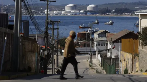 Un hombre es fotografiado caminando en la ciudad de Quintero con las empresas del cordon industrial de fondo, en Quintero (Agosto 2022)
