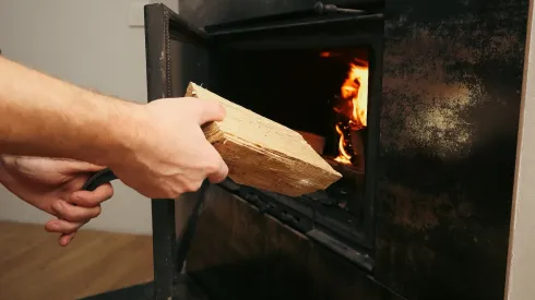 Persona carga leña en una chimenea encendida.
