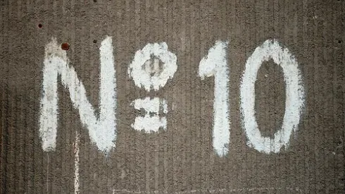 Large number sign with a capital N and the number 10 painted in white on an old building wall with a distinctive texture.