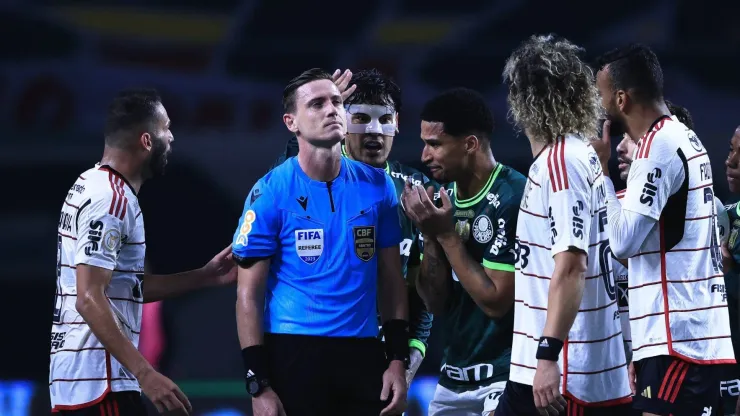 Imagem do árbitro sendo questionado em campo.
