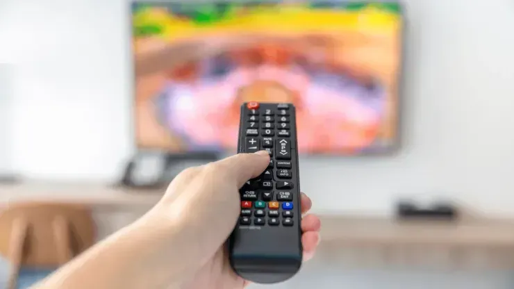 Mão feminina segura um controle remoto e o aponta a uma TV