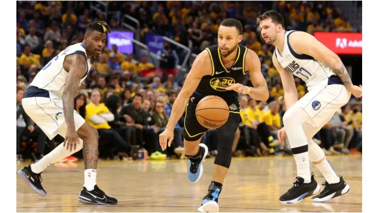 Stephen Curry #30 of the Golden State Warriors drives past Reggie Bullock #25 and Luka Doncic #77 of the Dallas Mavericks
