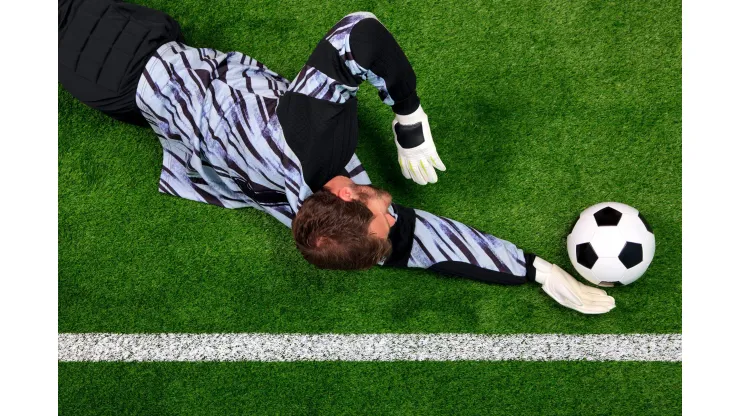 C8N32G Overhead photo of a football goalkeeper diving to save the ball from crossing the goal line.
