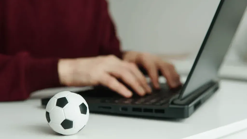 Imagem parcial de pessoa a trabalhar em laptop, com bola de futebol pequena junto do teclado