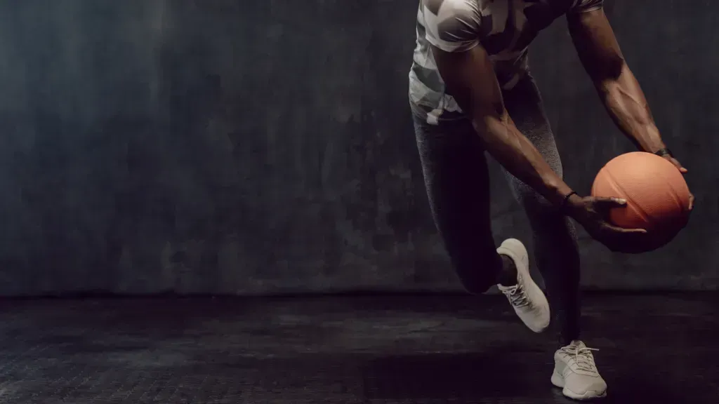 Imagem com fundo cinza e, do lado direito, atleta com equipamento de treino segura bola de basquete