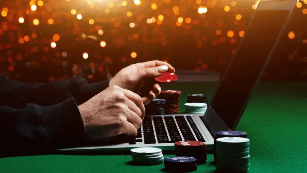 Imagem composta de laptop com tela escura e mãos masculinas mexendo em fichas de poker