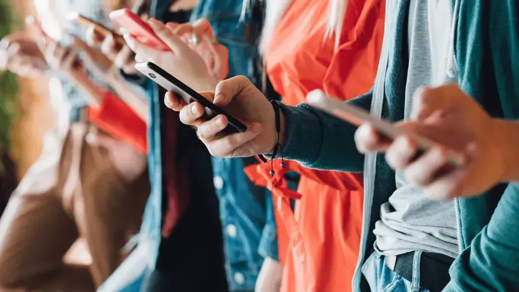 Imagem parcial de várias pessoas segurando o celular, as quais estão vestidas em tons de denim e vermelho