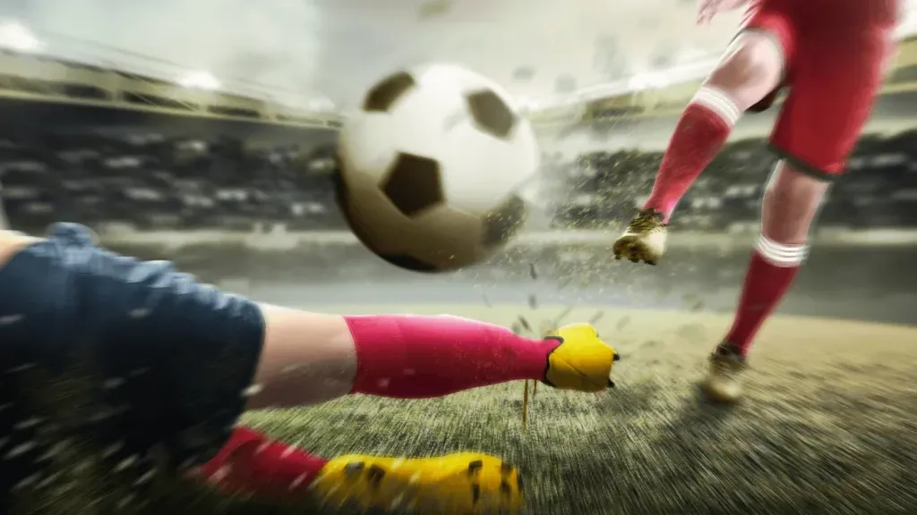 Imagem gráfica simulando dois jogadores em disputa pela clássica bola de futebol branca e preta. A bola está ao centro, o jogador da esquerda está no chão, enquanto o da direita corre em direção à bola.