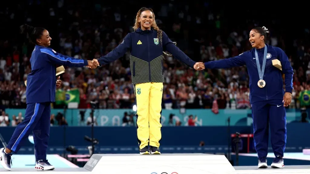 Gold medalist Rebeca Andrade (C) of Team Brazil, silver medalist Simone Biles (L) of Team United States and bronze medalist Jordan Chiles (R) of Team United States celebrate on the podium at the Artistic Gymnastics Women’s Floor Exercise Medal Ceremony. (Photo by Naomi Baker/Getty Images)