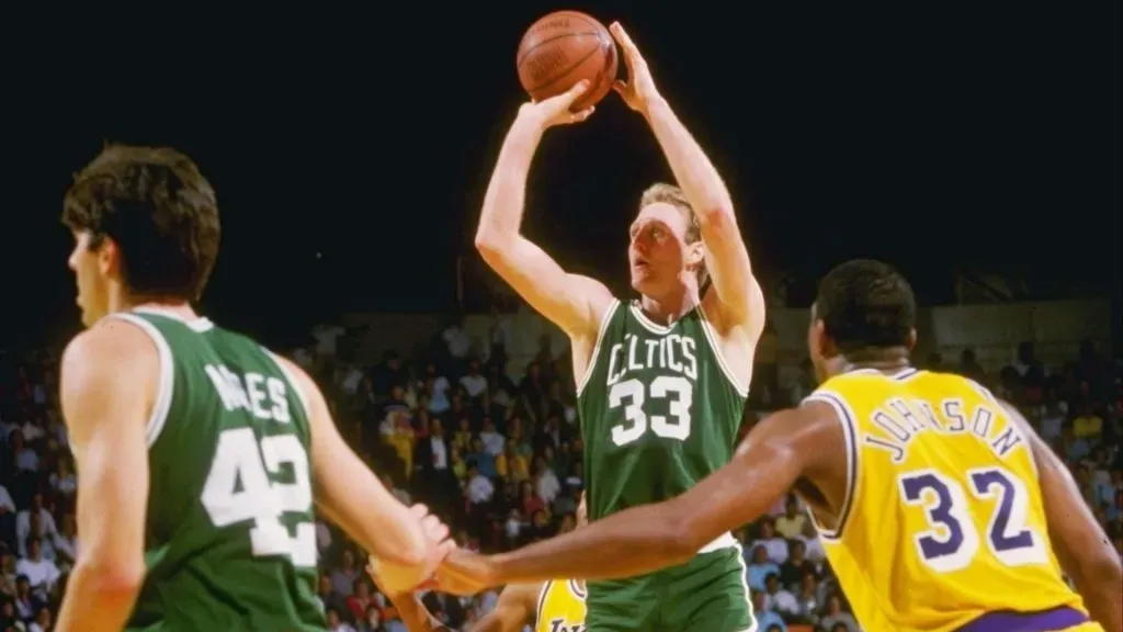 Larry Bird of the Boston Celtics shoots the ball as Magic Johnson of the Los Angeles Lakers watches him.