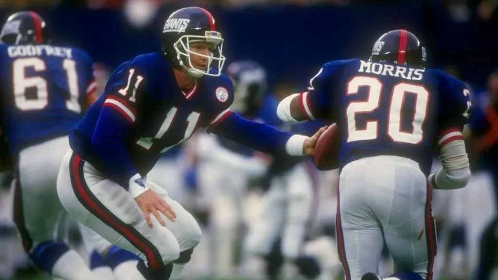 Quarterback Phil Simms of the New York Giants (left) hands off the ball to teammate running back Joe Morris during a game against the Green Bay Packers in 1986. (Source: Getty Images)