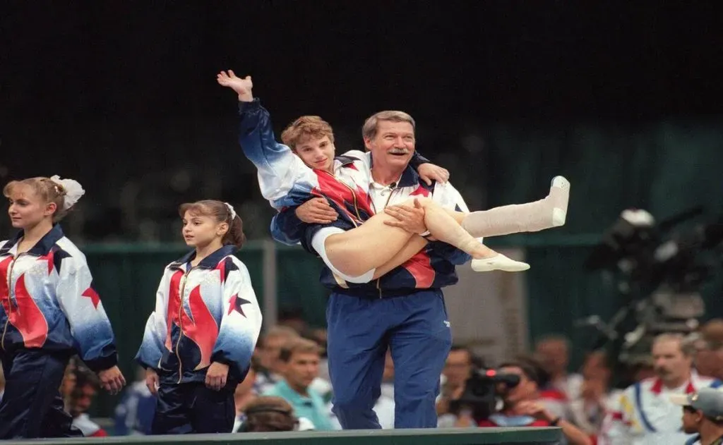 Kerri Strug, lesionada en su tobillo, es llevada por su entrenador luego de competir en Atlanta 1996. (Imago)