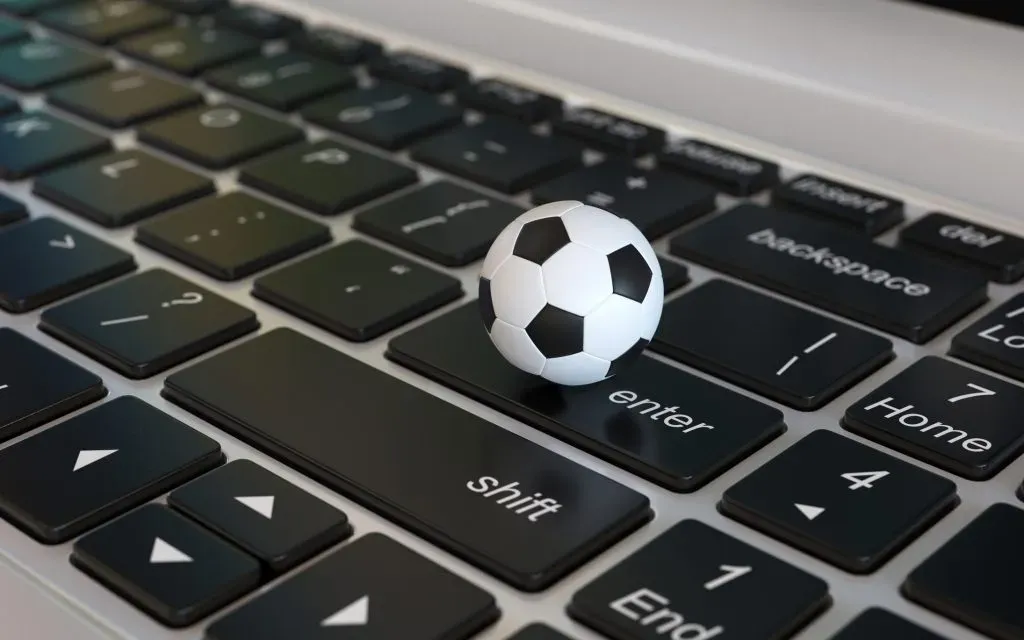 Miniatura de bola de futebol clássica, em branco e preto, em cima de teclado de notebook. 