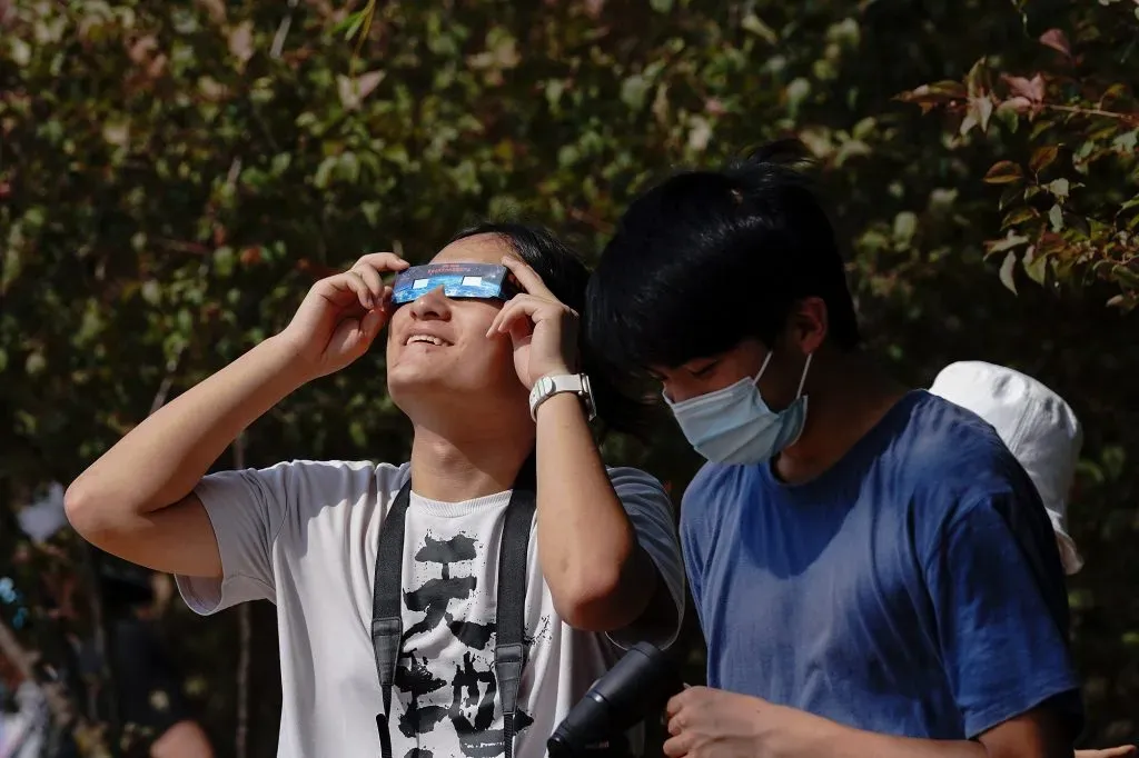 La gente mira a través de lentes protectores mientras observan el eclipse solar parcial en el parque olímpico el 21 de junio de 2020 en Beijing, China | Foto: Getty Images