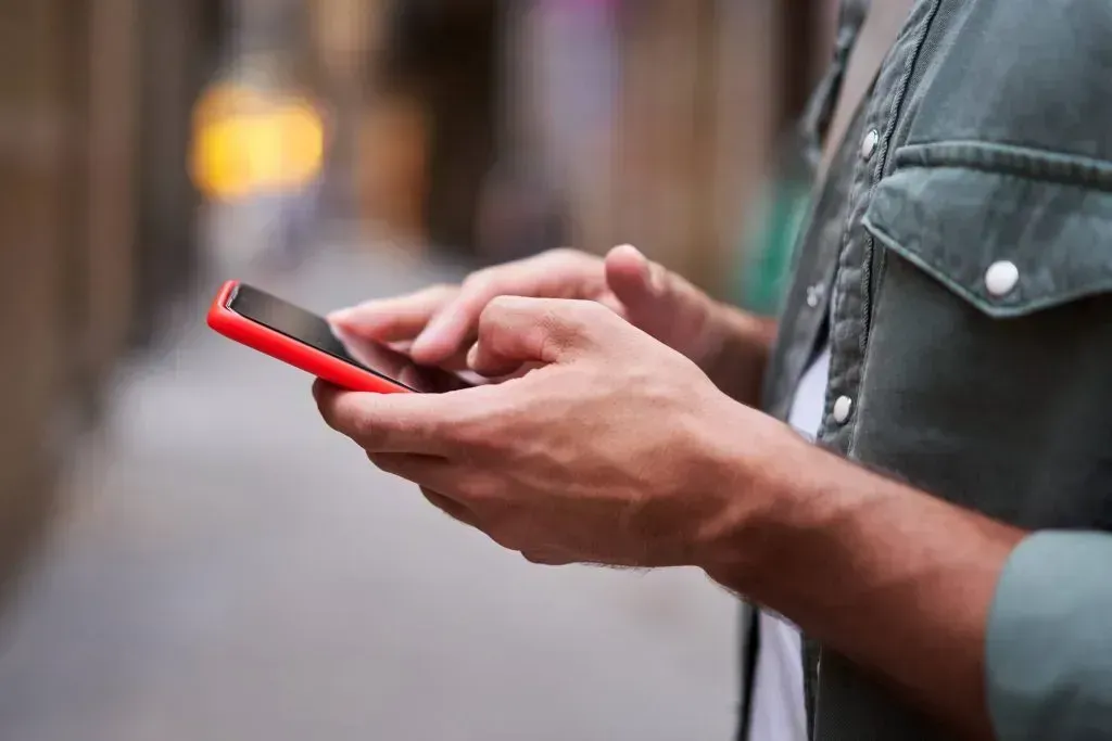 Imagem parcial de homem segurando celular com capa vermelha