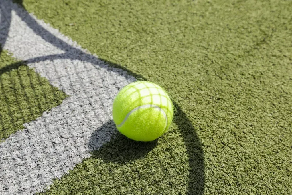 Bola de tênis sobre a linha de canto do campo, e sombra de uma raquete sobre os elementos.