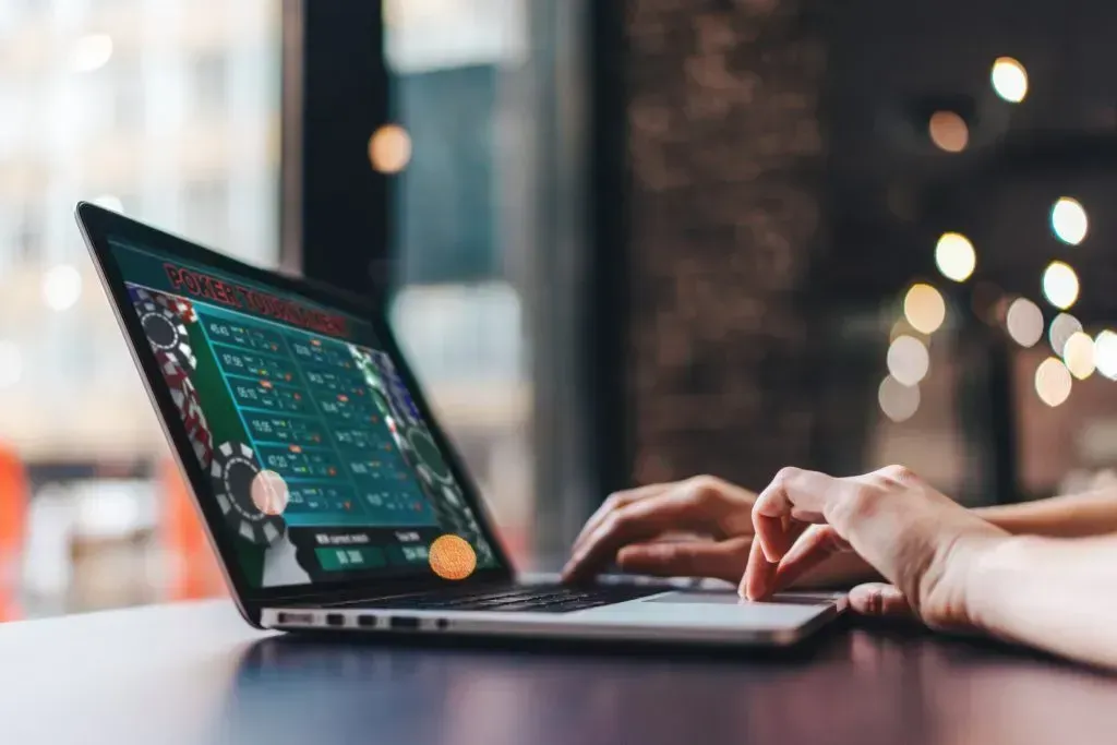 Duas mãos usam o teclado de um laptop onde decorre na tela um torneio de poker