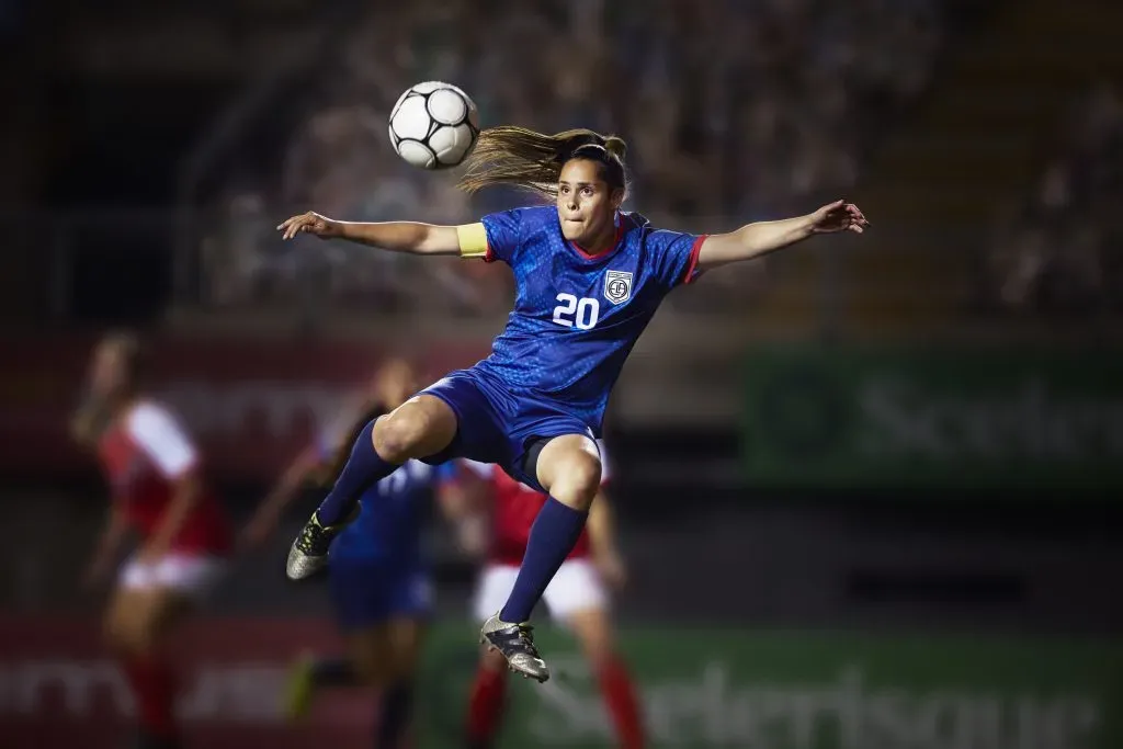 Action shot of a serious female football player as she jumps into the air to kick the soccer ball into the goal during a live game