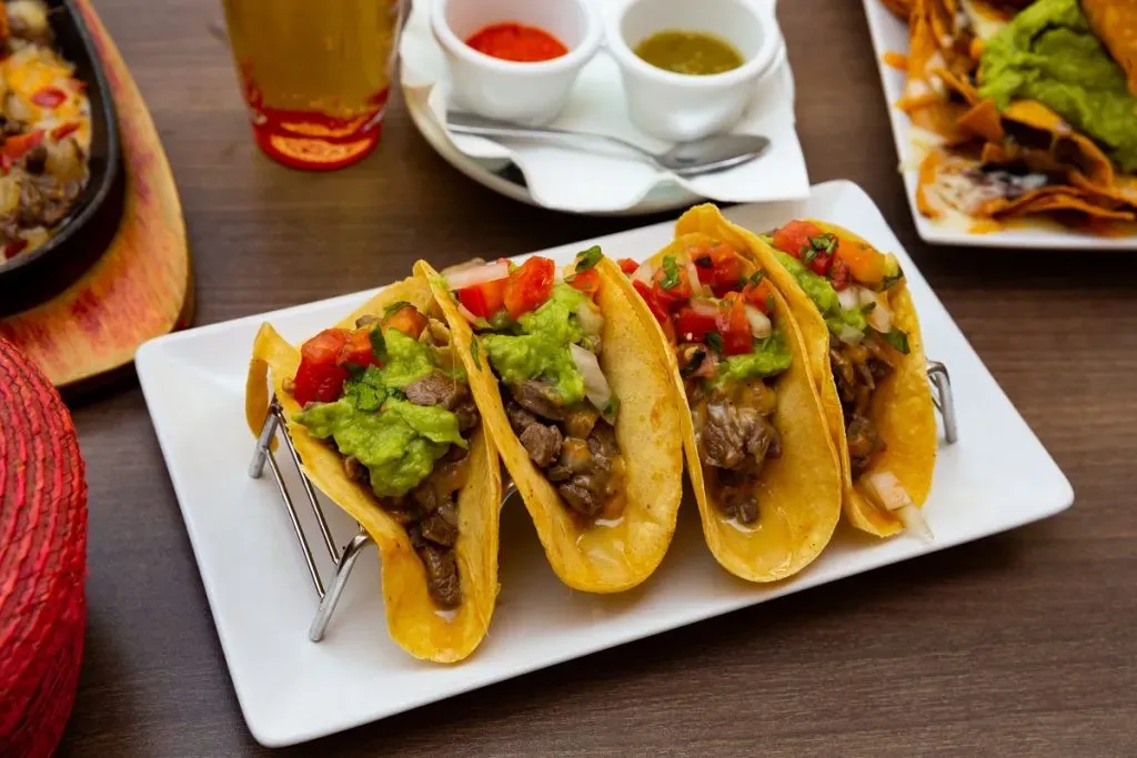 Cuatro tacos con carne, tomate y guacamole.