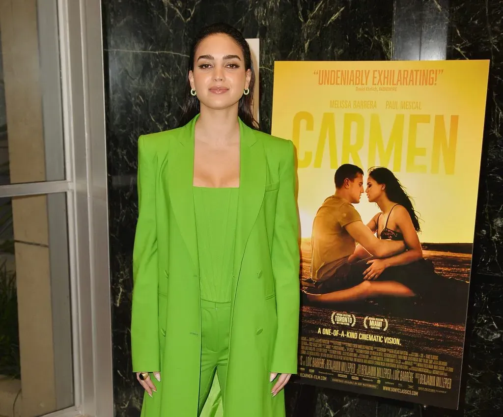 Melissa Barrera, posando al lado del poster promocional de Carmen, película que protagonizó 2022. Imagen: Getty Images.