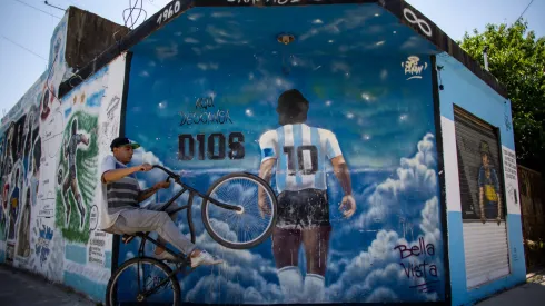 BUENOS AIRES, ARGENTINA - OCTOBER 21: A man wheelies past a mural depicting Diego Armando Maradona entering heaven with a legend that reads in spanish "Here rests god" making reference to the fact that the idol is buried one block away from the mural in Bella Vista on October 21, 2021 in Buenos Aires, Argentina. Football fans all over the country remember their late idol, who would have turned 61 on October 30. (Photo by Tomas Cuesta/Getty Images)