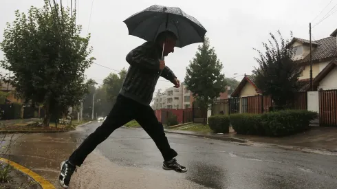Un transeúnte intenta cruzar un charco de agua durante sistema frontal que afecta a la región Metropolitana (16 de abril de 2016)