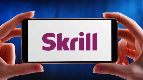 2C982EF POZNAN, POL – MAY 21, 2020: Hands holding smartphone displaying logo of Skrill (formerly Moneybookers), an e-commerce business that allows payments an