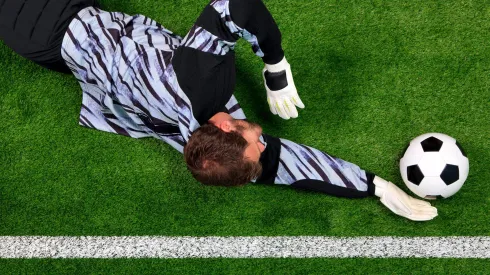 C8N32G Overhead photo of a football goalkeeper diving to save the ball from crossing the goal line.