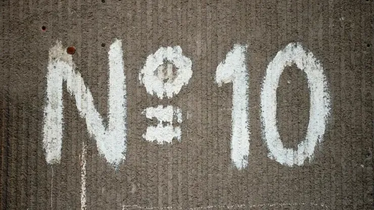 Large number sign with a capital N and the number 10 painted in white on an old building wall with a distinctive texture.
