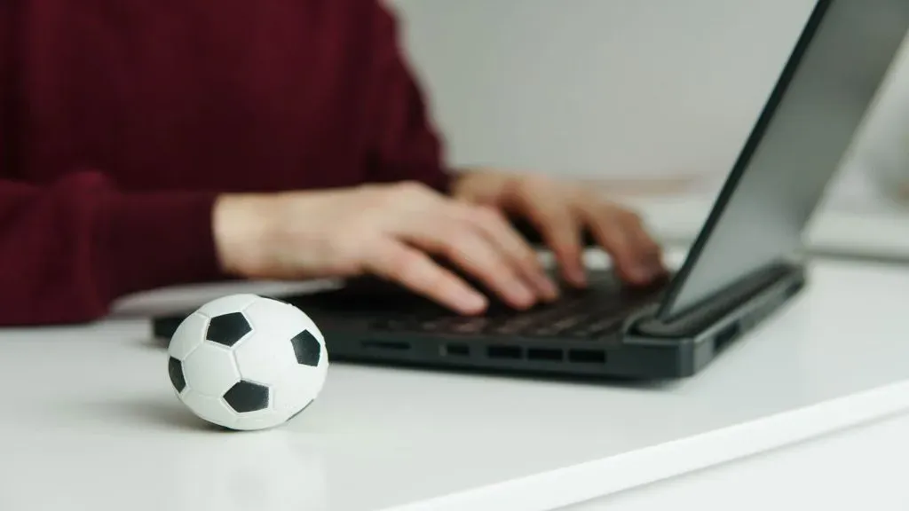 A imagem mostra uma pessoa usando um laptop para apostar na Copa América na Bet7k. Ao lado do laptop, há uma pequena bola de futebol.
