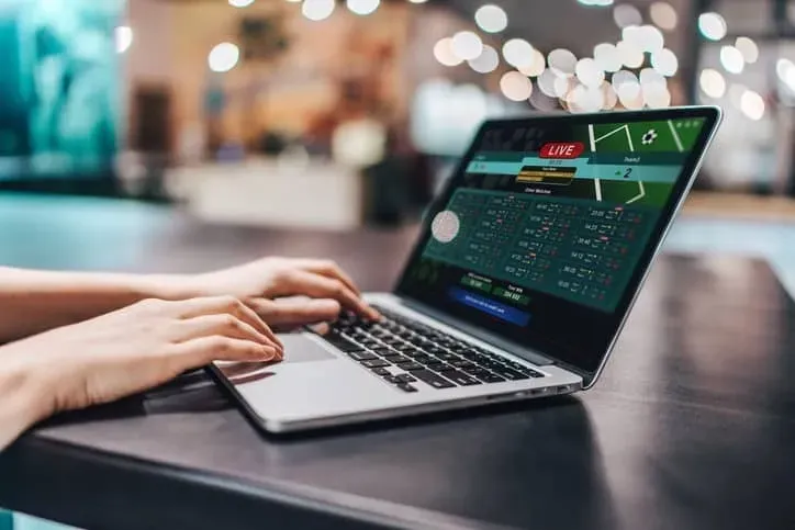 Foto de notebook aberto em site de casas de apostas com as mãos de usuário posando em cima do teclado.