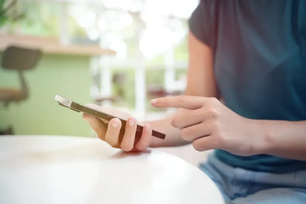 Imagem de torso e mãos de mulher segurando um smartphone.