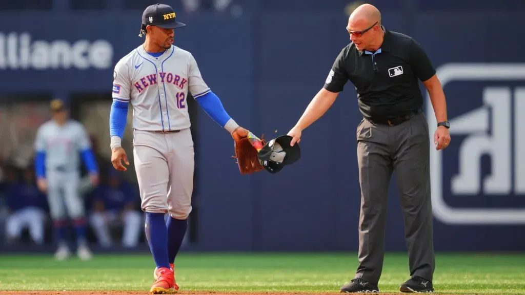 Francisco Lindor #12 of the New York Mets has a bee swatted off of his glove by umpire Stu Scheurwater in a break in play against the Toronto Blue Jays during the sixth inning in their MLB game. (Photo by Mark Blinch/Getty Images)