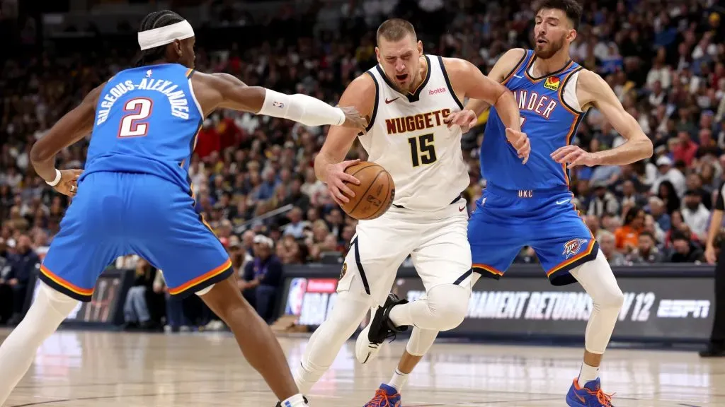 Nikola Jokic #15 of the Denver Nuggets drives against Shai Gilgeous-Alexander #2 and Chet Holmgren #7 of the Oklahoma City Thunder in the first quarter at Ball Arena on October 24, 2024 in Denver, Colorado.