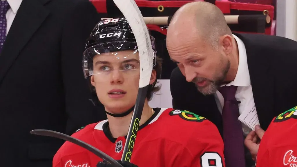 Chicago Blackhawks interim coach Anders Sorensen speaks with center Connor Bedard in the bench during an NHL game.