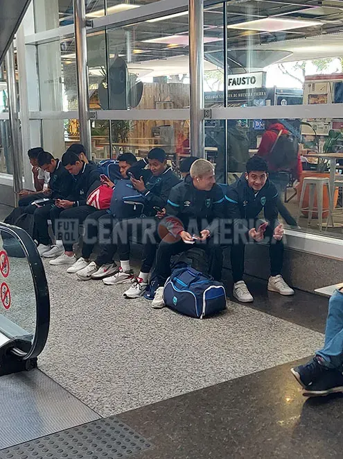 Algunos futbolistas de la delegación esperan sentados a que sus compañeros terminen con el check-in