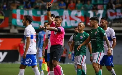 Nicolás Gamboa muestra una de las cuatro tarjetas rojas para futbolistas en el duelo que la UC le ganó al Audax Italiano. (Agencia Uno).