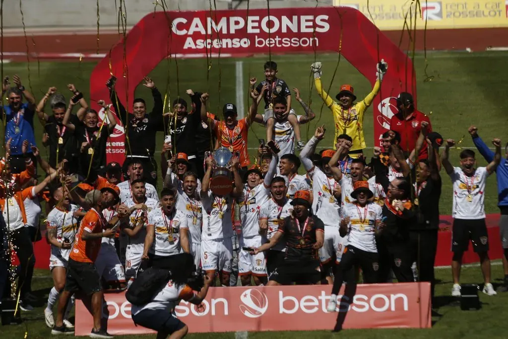 Hugo Araya festeja con los brazos arriba, de uniforme amarillo y con un gorro naranja, el histórico ascenso de Cobreloa a la primera división. (José Robles/Photosport).