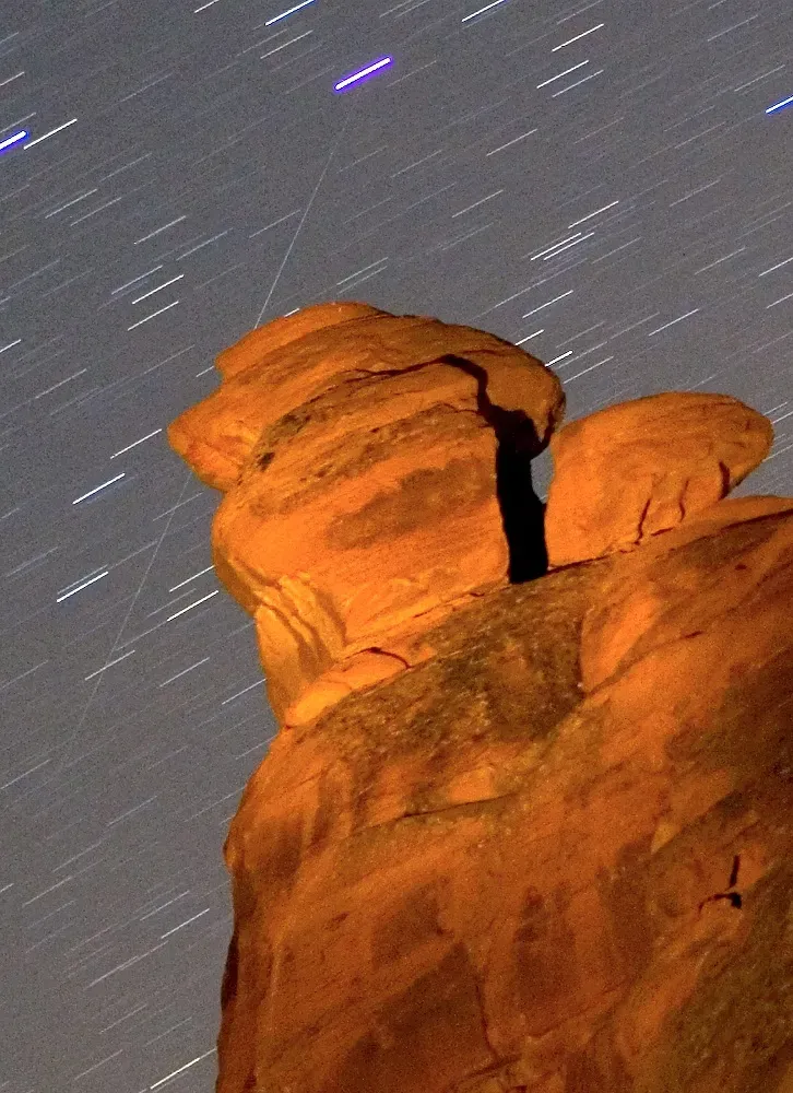 Un meteoro de las Gemínidas cruza diagonalmente el cielo contra un campo de estrellas detrás de la formación rocosa de Seven Sisters.