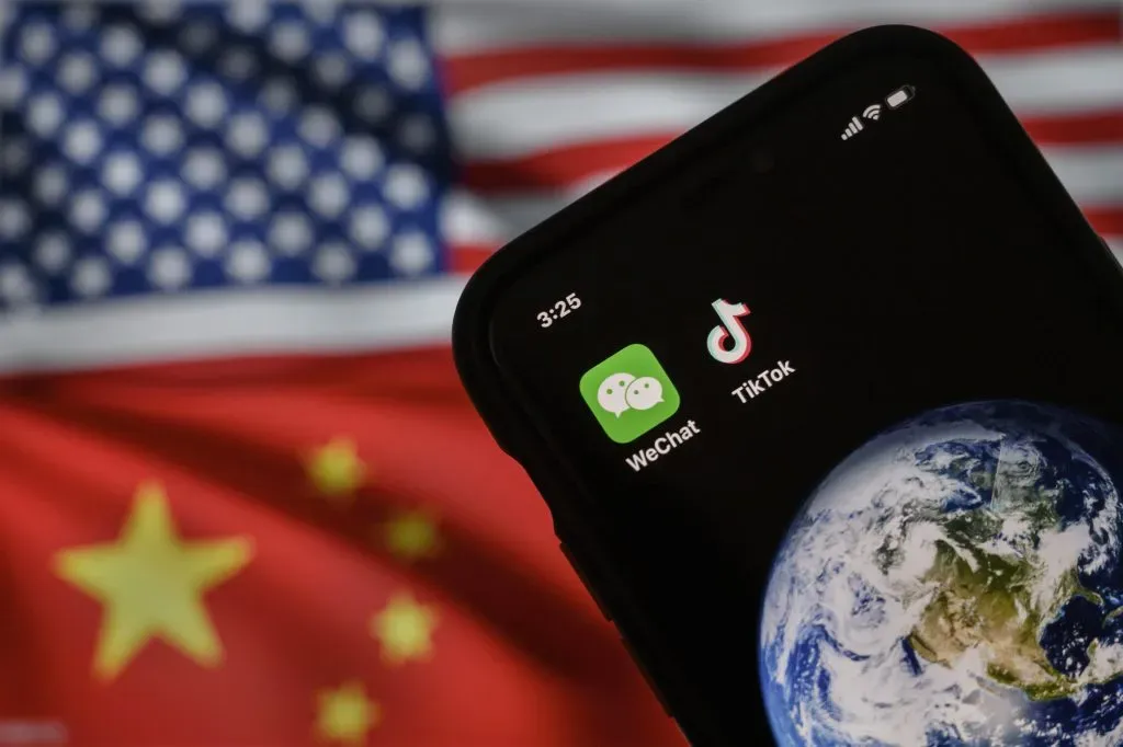 BEIJING, CHINA – SEPTEMBER 22: In this photo illustration, a mobile phone can be seen displaying the logos for Chinese apps WeChat and TikTok in front of a monitor showing the flags of the United States and China on an internet page, on September 22, 2020 in Beijing, China. Both popular Chinese-owned apps are facing bans under an executive order signed by United States President Donald Trump, but on Saturday, Trump said he was giving the go ahead to a deal between TikTok, Oracle, and Walmart and a judge in California issued a preliminary injunction blocking the administrations WeChat ban. (Photo by Kevin Frayer/Getty Images)