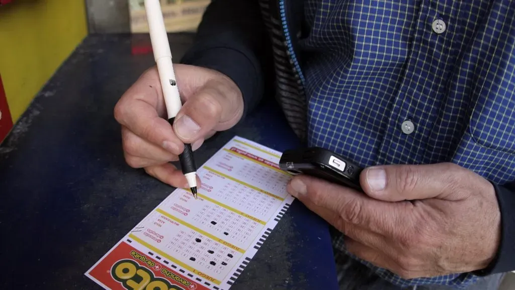 Una persona jugando al Loto, mientras marca sus número preferidos en un cartón.