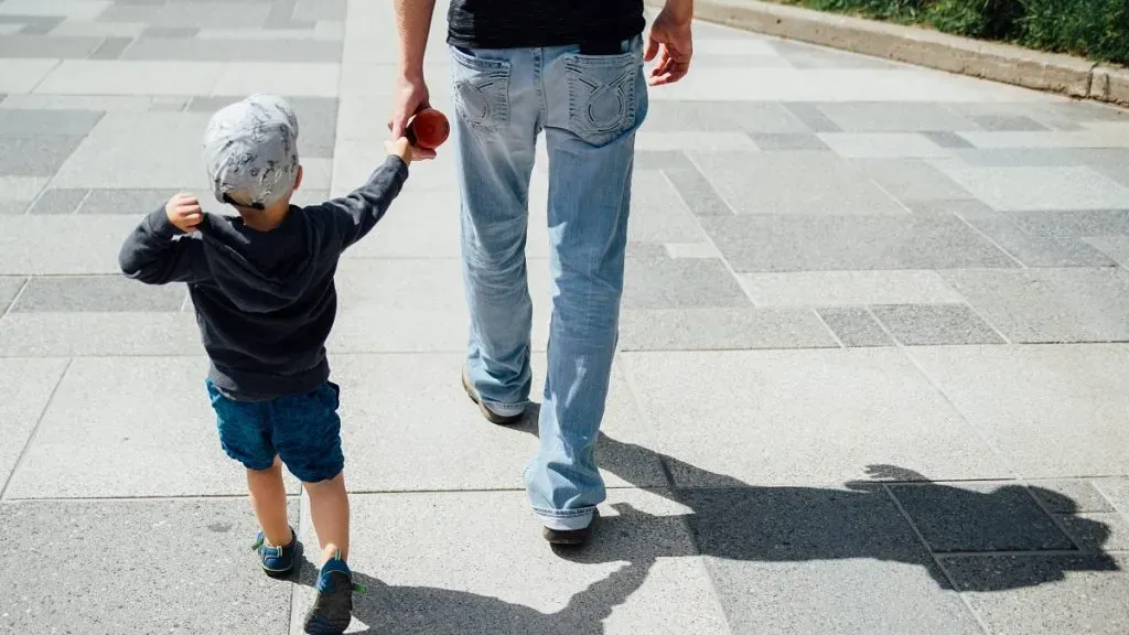Padre camina de la mano con su pequeño hijo.