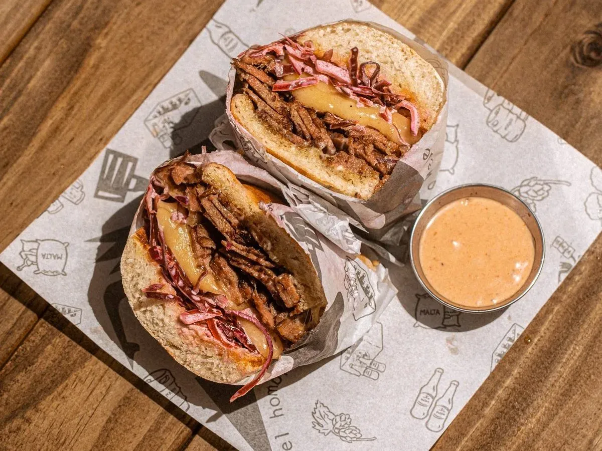 Plato El Rubén, un sándwich de brisket ahumado con coleslaw picante, queso gouda, mayonesa de la casa, salsa especial en pan ciabatta tostado, y pepinillo dill.